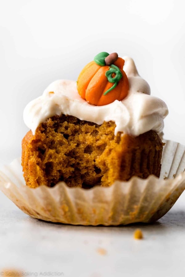 a bite taken out of a pumpkin cupcake topped with cream cheese frosting